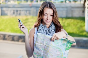 young woman tourist holding paper map outdoors and talking by th